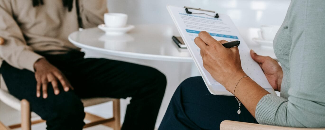 Two professionals engaged in a consultation, one taking notes on a clipboard.